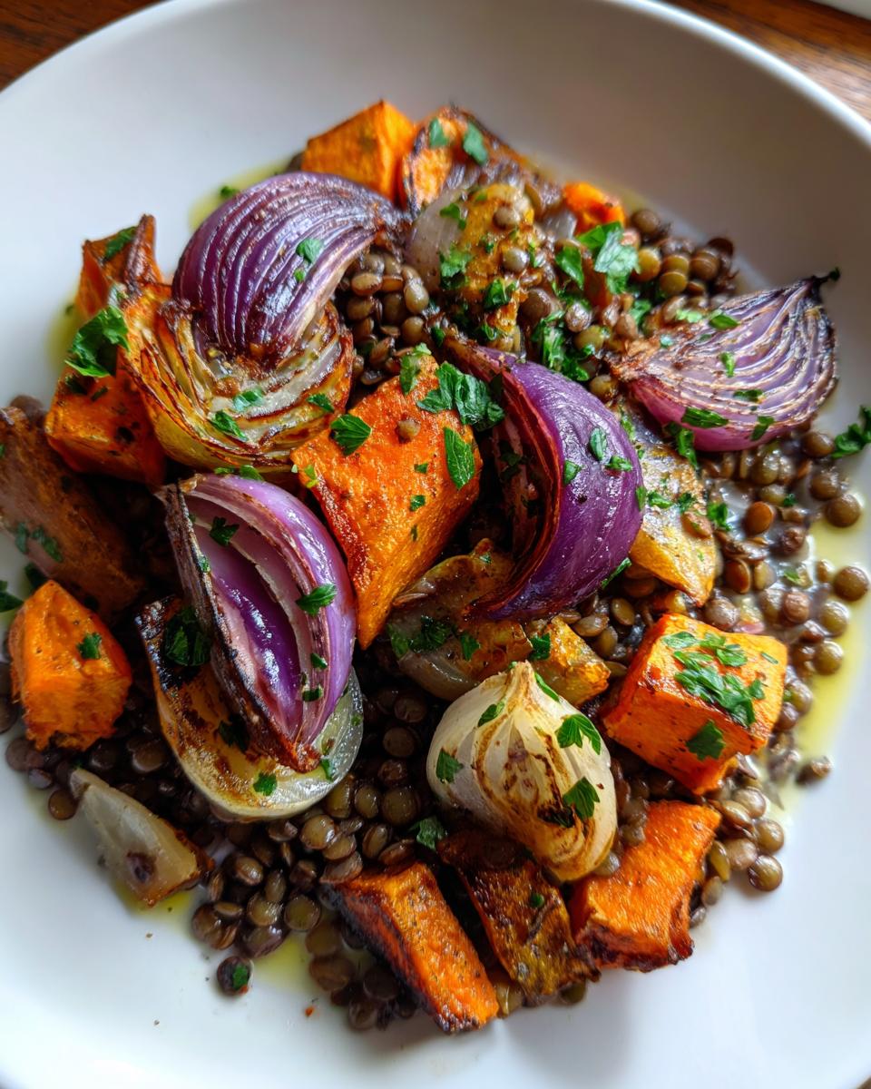 Close-up of a bowl featuring a hearty veggie lentil salad with roasted sweet potatoes, red onions, and garlic.