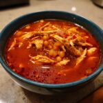 Close-up of a vibrant bowl of red chicken pozole featuring shredded chicken and hominy in a rich broth.