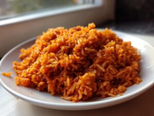 A close-up shot of vibrant, orange-red jollof rice piled high on a white plate, ready to eat.
