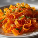 Close-up of a vibrant raw carrot salad featuring shaved carrot ribbons, topped with toasted sesame seeds and green onion slivers.