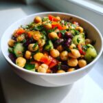 A vibrant bowl of 15-Minute bean salad featuring chickpeas, kidney beans, cucumber, and red pepper, garnished with parsley.