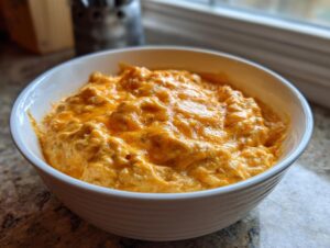 Close-up of a white bowl filled with creamy, orange chili cheese dip topped with melted cheddar cheese.