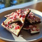 Stacked pieces of dark and white chocolate peppermint bark topped with crushed candy canes.