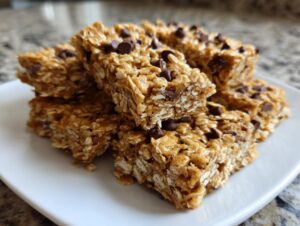 A stack of homemade, chewy protein bars featuring oats and mini chocolate chips, served on a white plate.
