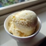 A close-up of a creamy scoop of homemade banana ice cream served in a white bowl near a sunlit window.
