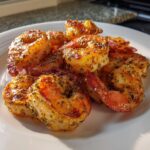 A pile of perfectly cooked, seasoned air fryer frozen shrimp on a white plate, showing crispy edges.