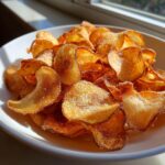 A white bowl filled with golden brown, perfectly crispy air fryer potato chips sprinkled with salt.