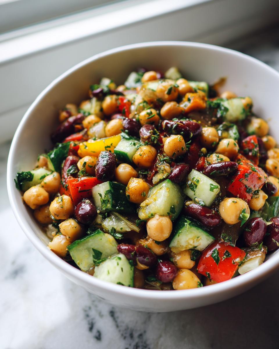 Close-up of a fresh bean salad featuring chickpeas, kidney beans, cucumber, and red pepper, tossed in herbs.
