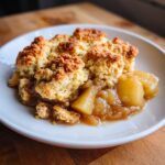 Close-up of a warm serving of apple cobbler with a golden, crumbly topping and soft, spiced apple filling.