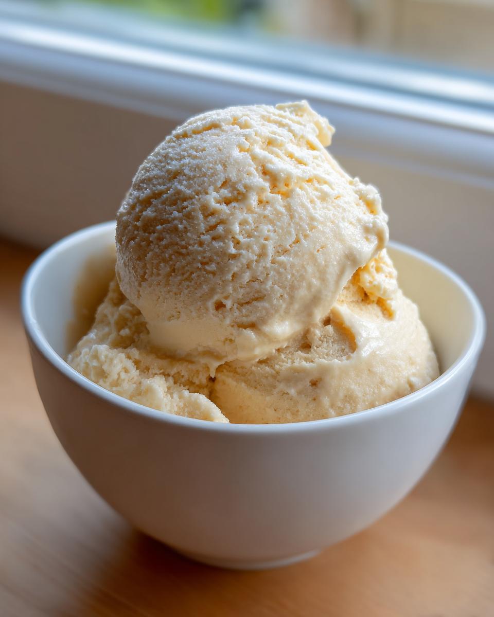 Close-up of two scoops of creamy, pale yellow banana ice cream served in a white bowl.