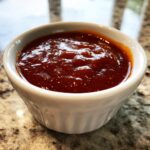 A close-up shot of thick, rich, homemade bbq sauce filling a small white ramekin.