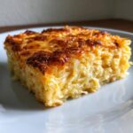A close-up of a baked slice of cheesy potato casserole with a golden-brown, bubbly top.