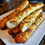 A stack of golden brown, fluffy copycat breadsticks seasoned with garlic, Parmesan, and parsley, served on a white plate.