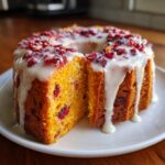 A slice cut from a moist cranberry orange cake topped with white glaze and dried cranberries.