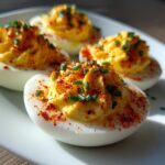 Close-up of four creamy deviled eggs topped with paprika and fresh chives on a white plate.