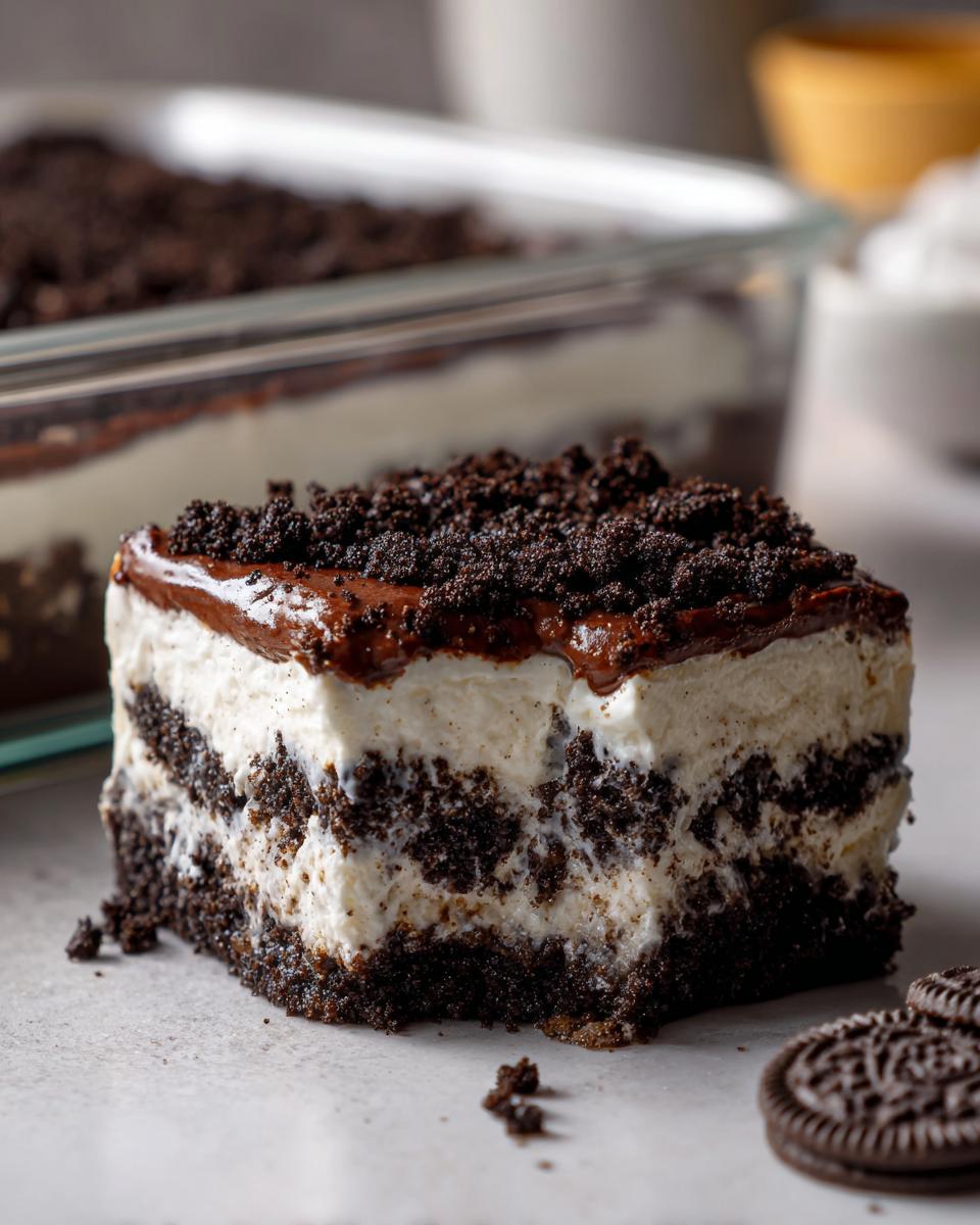 A square slice of amazing dirt cake showing layers of chocolate cookie crumbs and cream filling, topped with fudge.