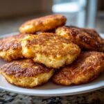 A close-up stack of golden brown, perfectly fried cornbread rounds on a white plate.
