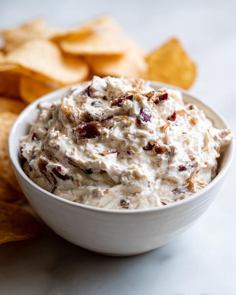A white bowl filled with creamy onion dip mixed with caramelized onions, served with tortilla chips.
