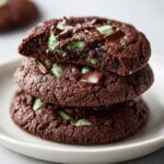 Close-up of a stack of three rich, dark chocolate Andes Mint Cookies, one broken open to show the minty green center.