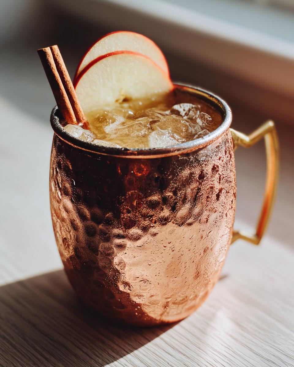 Close-up of a frosty apple cider moscow mule garnished with apple slices and a cinnamon stick.