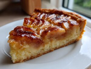 Close-up of a thick slice of glazed apple tart showing caramelized apples and a rich base, ready to eat.