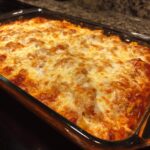 Close-up of a bubbly, cheesy baked chicken enchilada dip in a clear glass casserole dish.