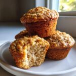 A stack of golden brown banana oatmeal muffins, one broken open to show the moist interior.