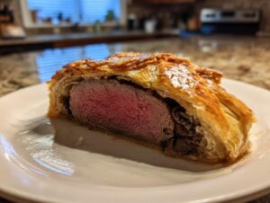 A cross-section slice of beef wellington recipe showing medium-rare pink tenderloin wrapped in golden puff pastry and duxelles.