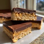 Three layered bars, resembling buckeye graham crackers, featuring a crust, peanut butter filling, and chocolate topping.