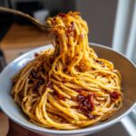 A fork lifting a generous twirl of spaghetti from a bowl of rich, golden caramelized onion pasta.