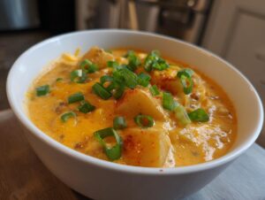 Close-up of a white bowl filled with creamy, cheesy cheeseburger soup topped with green onions.