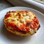 A single, perfectly toasted half of a pizza bagel topped with bubbling red sauce and melted, browned mozzarella cheese.