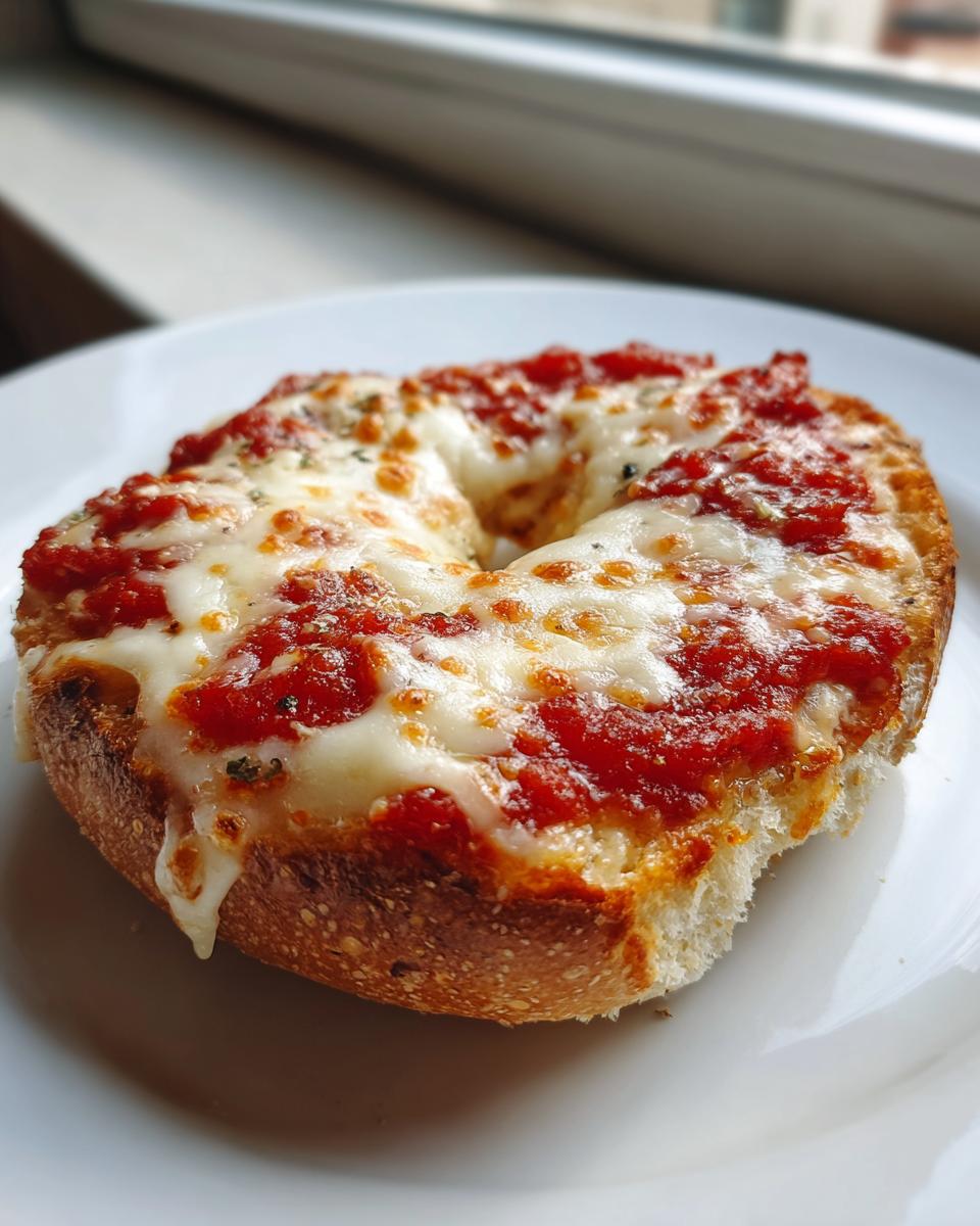 A close-up of a perfectly melted pizza bagels half topped with rich tomato sauce and gooey mozzarella cheese.