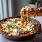 A spoonful of cheesy, meaty skillet lasagna is lifted, showing long, dramatic cheese pulls over the rest of the dish.