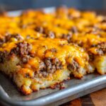 A close-up view of baked Cheesy Taco Potatoes layered with ground beef and melted cheddar cheese in a metal baking sheet.
