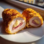 Two halves of crispy, golden-brown chicken cordon bleu showing melted cheese and ham filling inside.
