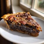 A close-up, sunlit slice of rich chocolate bourbon pecan pie showing gooey filling and pecan topping.