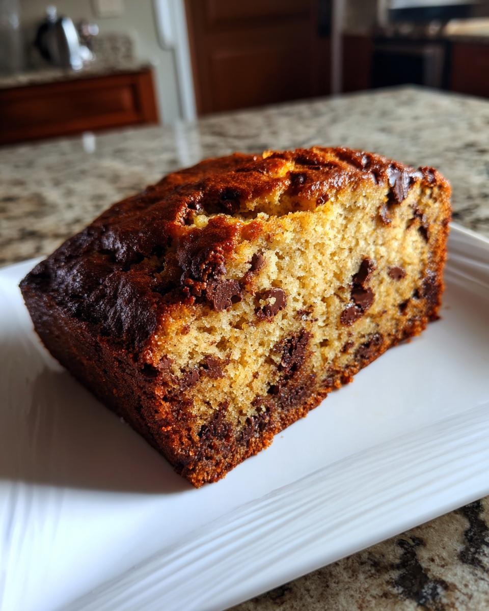 A thick slice of moist banana bread recipe studded with chocolate chips, served on a white plate.