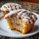 Close-up of a cinnamon roll muffin with a bite taken out, showing the swirl and topped with white glaze.
