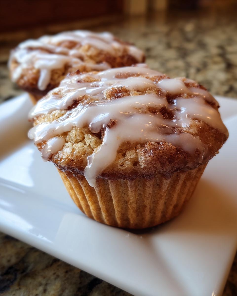 Close-up of a freshly baked cinnamon roll muffin topped with a thick white glaze.