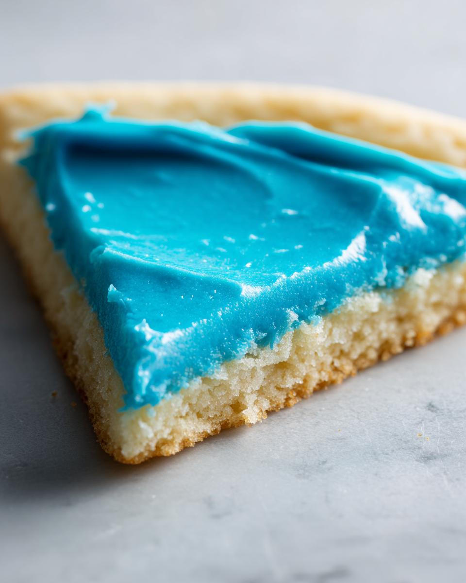 A close-up, macro shot of a slice of sugar cookie topped with thick, vibrant blue cookie icing recipe.