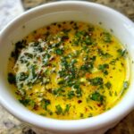 Close-up of melted butter infused with garlic, parsley, and red pepper flakes, ready to serve as cowboy butter dipping sauce.
