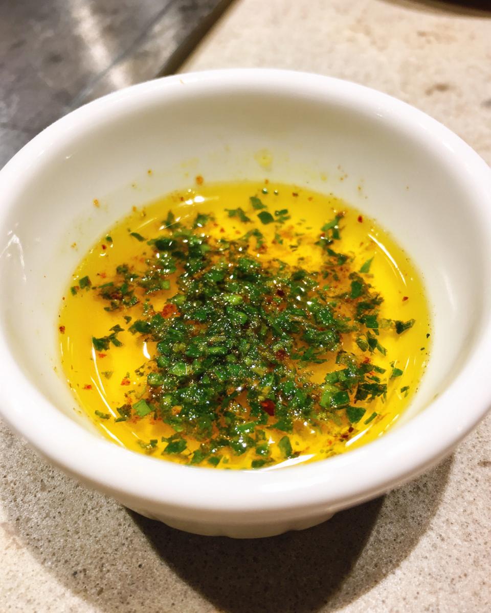 Close-up of melted butter topped with fresh green herbs and red pepper flakes, ready to serve as cowboy butter dipping sauce.