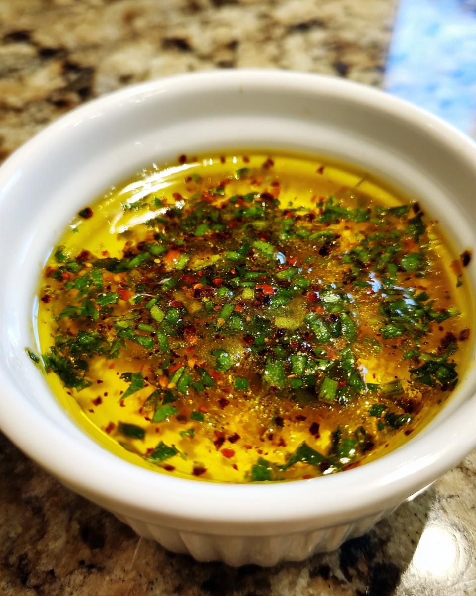 Close-up of vibrant yellow cowboy butter dipping sauce topped with green herbs and red pepper flakes in a white bowl.