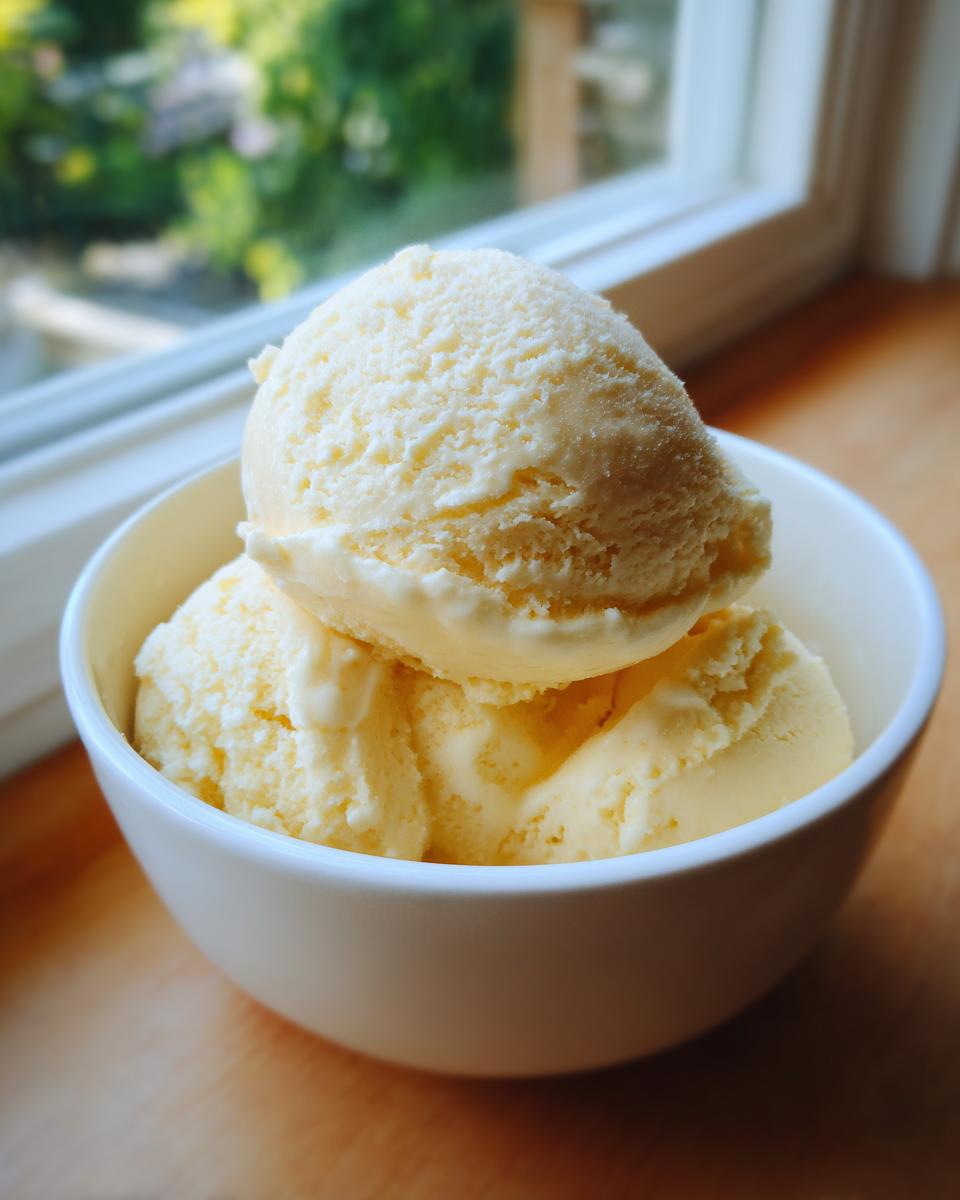 Close-up of three scoops of pale yellow banana ice cream served in a white bowl near a window.