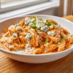 A close-up of creamy buffalo chicken chili topped with blue cheese crumbles and green onions.