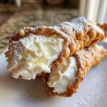Two freshly filled cannoli pastries dusted with powdered sugar, showcasing the creamy ricotta filling from our cannoli recipe.