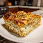 A close-up of a thick, creamy slice of chicken lasagna featuring layers of pasta, white sauce, and shredded chicken, topped with browned cheese.