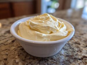 A close-up of thick, creamy homemade mayonnaise swirled high in a small white bowl on a granite countertop.