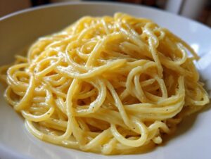 A close-up shot of perfectly coated spaghetti noodles in a rich, creamy lemon pasta sauce, served in a white bowl.